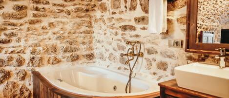 A stone-walled bathroom with a freestanding bathtub, wooden vanity, and a mirror.