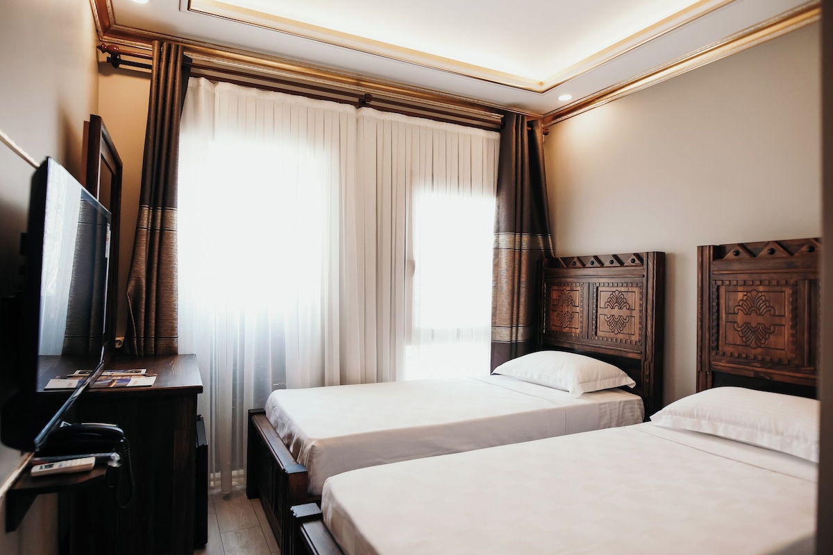 A hotel room with two beds, a desk, and a television.