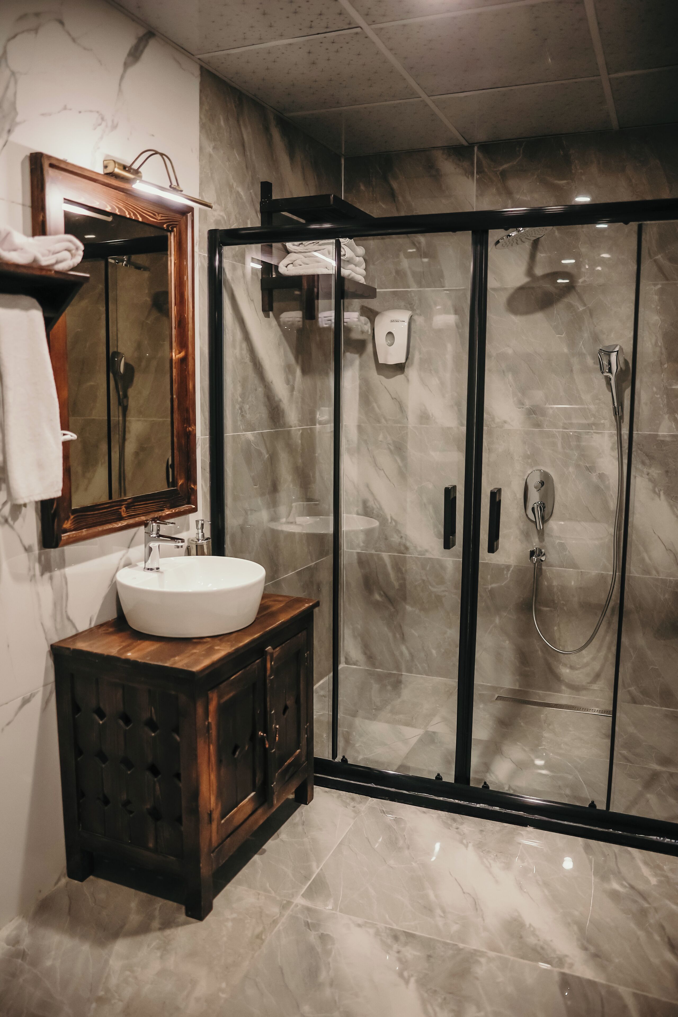 A modern bathroom with a marble sink, a wooden vanity, a glass-enclosed shower, and a large mirror.