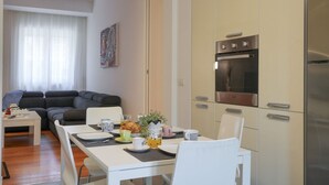 Una cocina moderna con horno y refrigerador integrados, una mesa de comedor con sillas, un sofá y un cuadro en la pared.