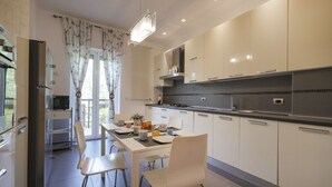 Una cocina moderna con armarios blancos, una mesa de comedor con sillas y un gran ventanal con cortinas.