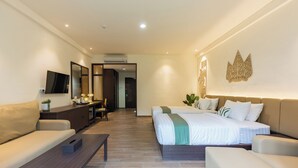 Una habitación de hotel moderna con un sofá, una cama con edredón verde y blanco, un escritorio con computadora y un televisor montado en la pared.