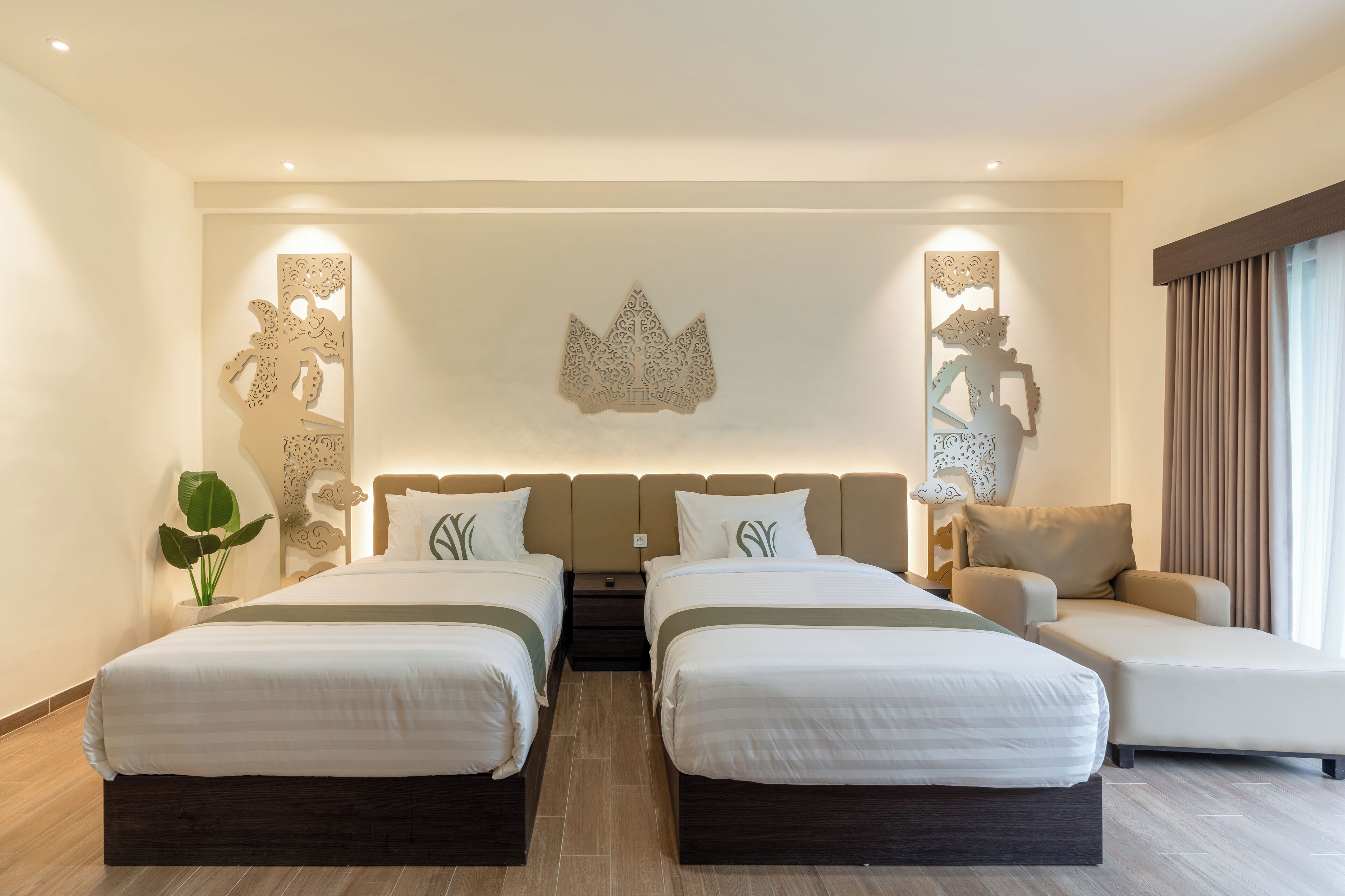 A hotel room with two beds, a sofa, decorative wall art, and a plant.