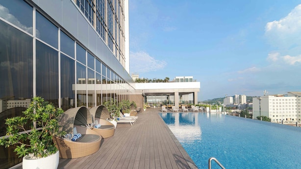 A rooftop infinity pool with wooden decking and lounge chairs, surrounded by modern buildings. - Oakwood Hotel & Apartments Grand Batam (Batam)