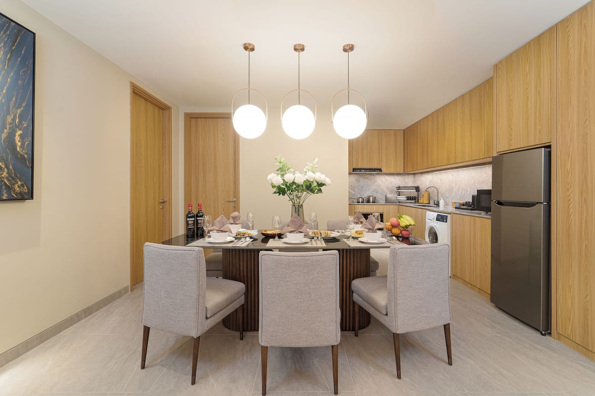 Een moderne keuken met houten kastjes, een roestvrijstalen koelkast en een eethoek met een ronde tafel en vier stoelen.