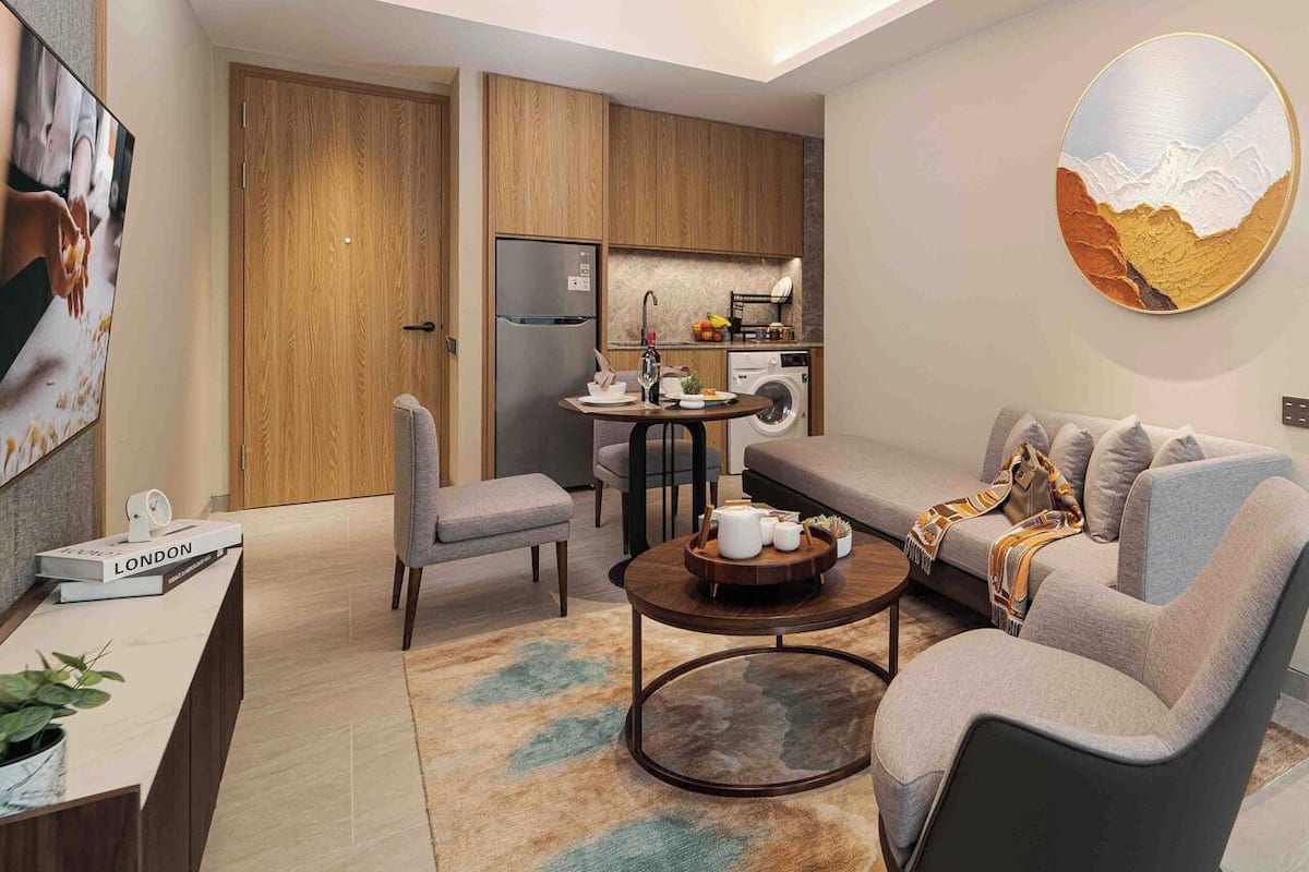 Een moderne woonkamer met een bank, fauteuils, een salontafel en een keukenhoek met een koelkast en spoelbak.