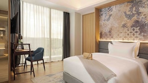 A modern hotel room with a large bed, a desk with a chair, a TV, and a large window with curtains. - Oakwood Hotel & Apartments Grand Batam (Batam)