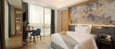 A hotel room with a large bed, a desk with a chair, a nightstand, and a large window with curtains.