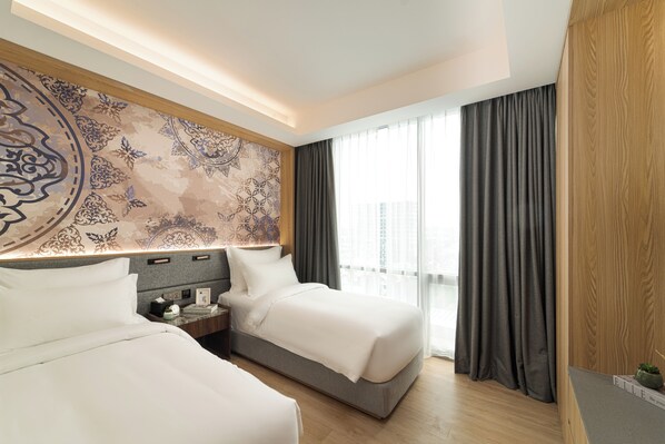 A hotel room with two beds, a large patterned wall, a nightstand, and a view of the city through large windows.