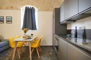 A compact kitchen with modern appliances, a dining area with yellow chairs, and a stone wall.