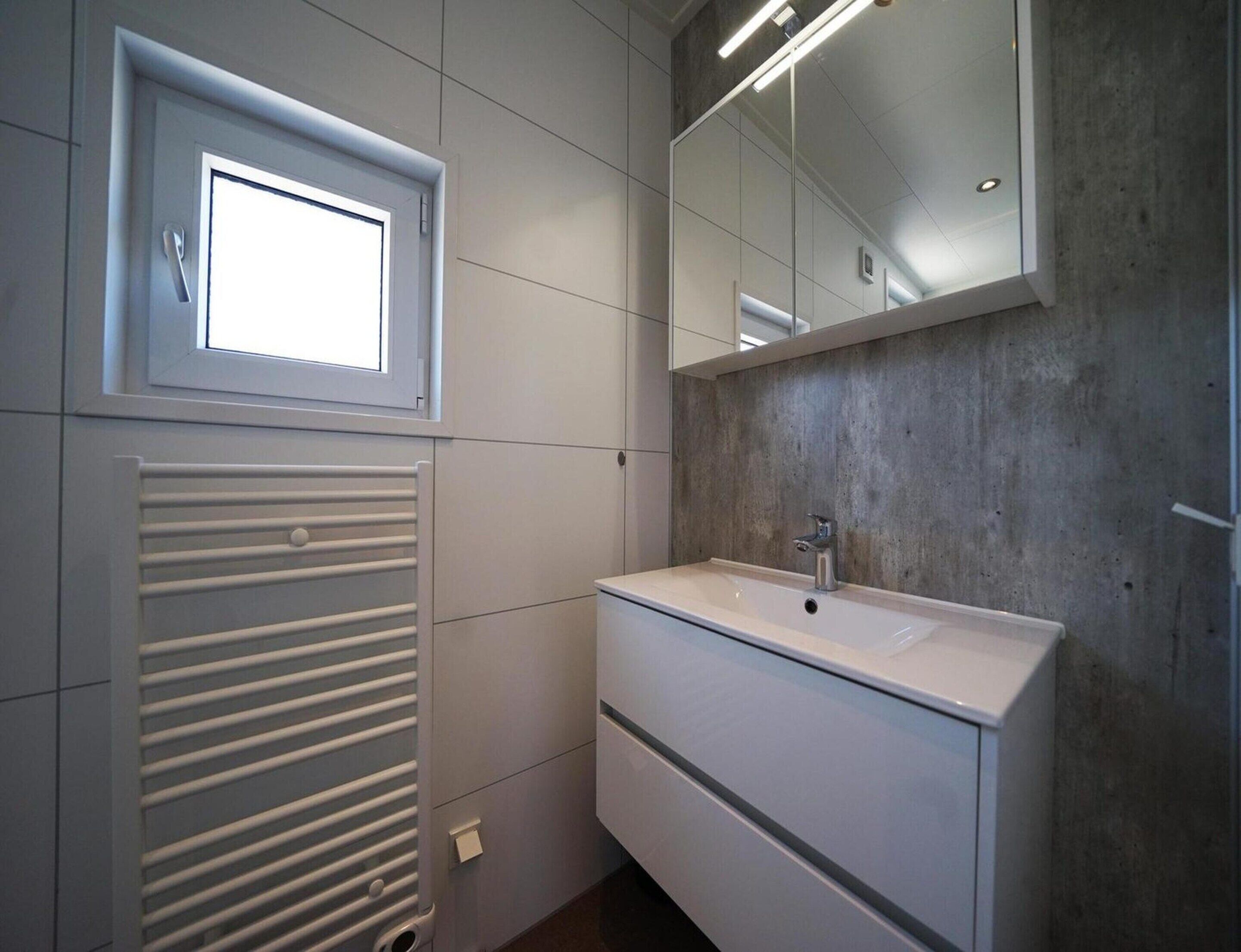 A bathroom with a window, a sink, a mirror, and a radiator.