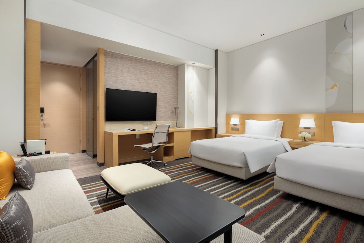A hotel room with a bed, a desk, a chair, a TV, and a small table.