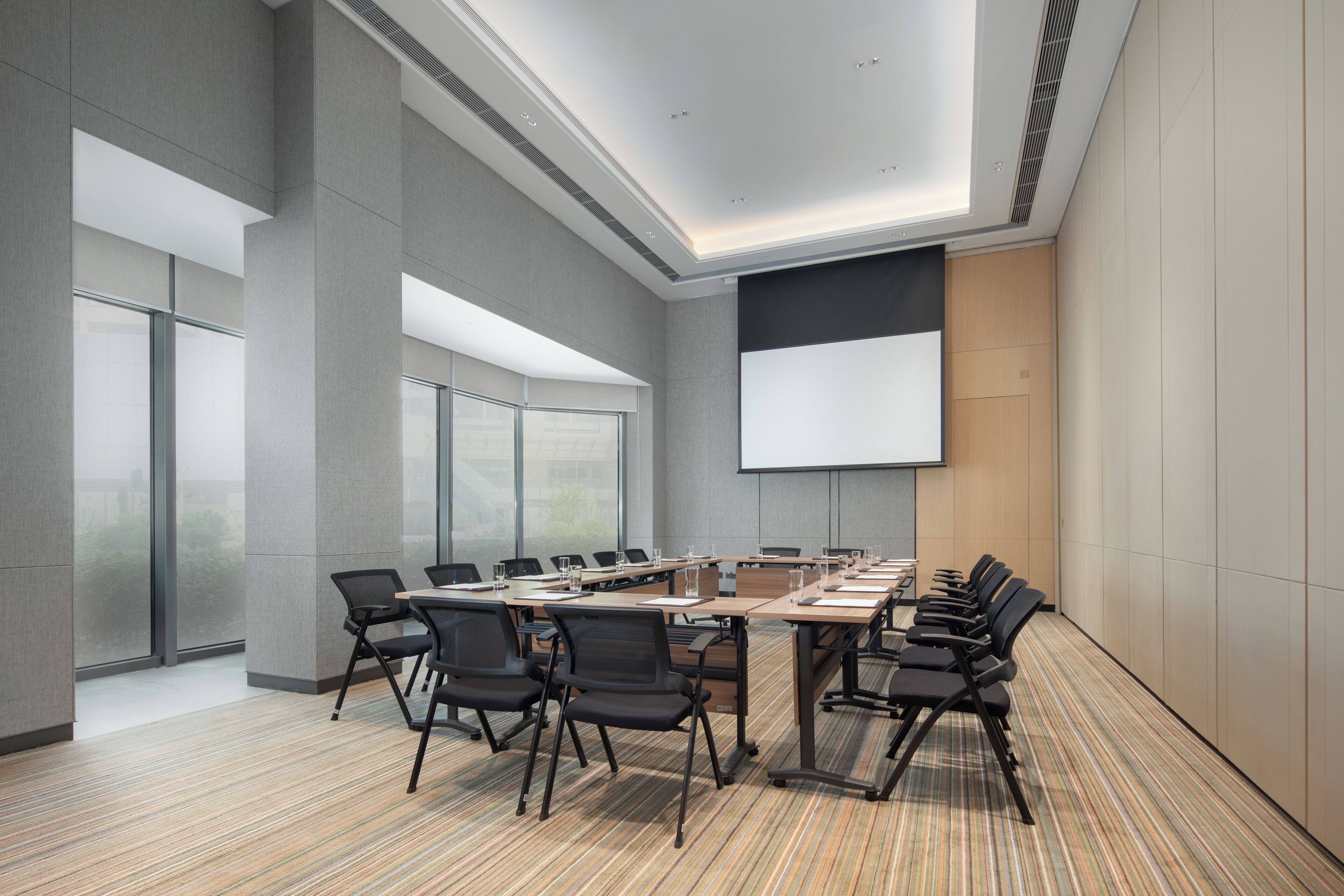 A conference room with a large table, chairs, a projector screen, and large windows.
