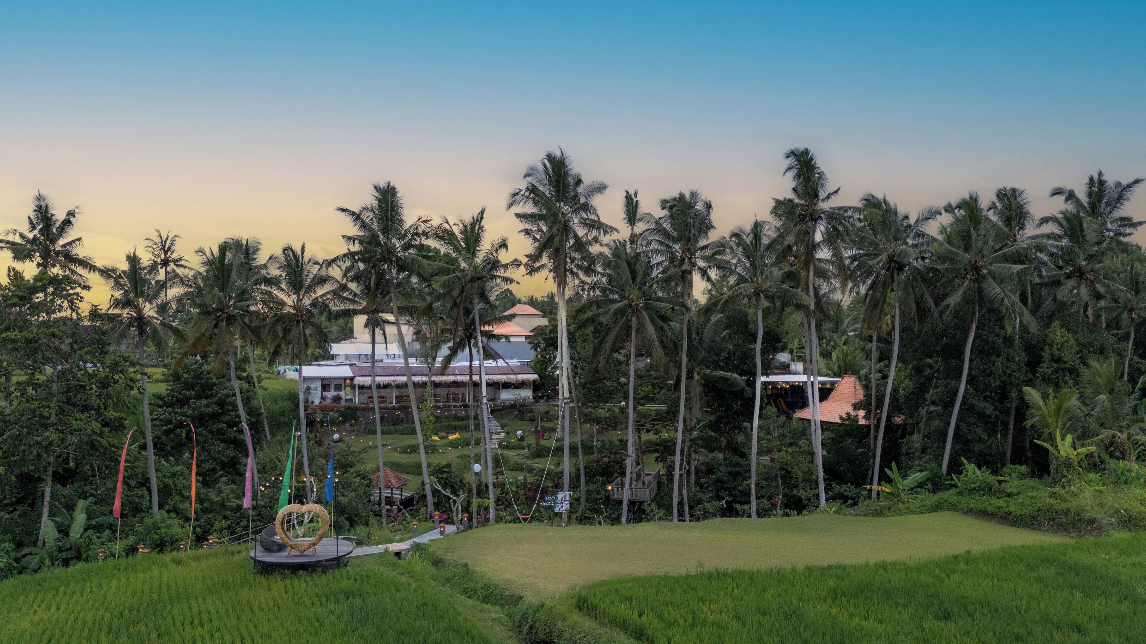 Un resort tropical con una construcción de techo de paja, palmeras y un área verde.