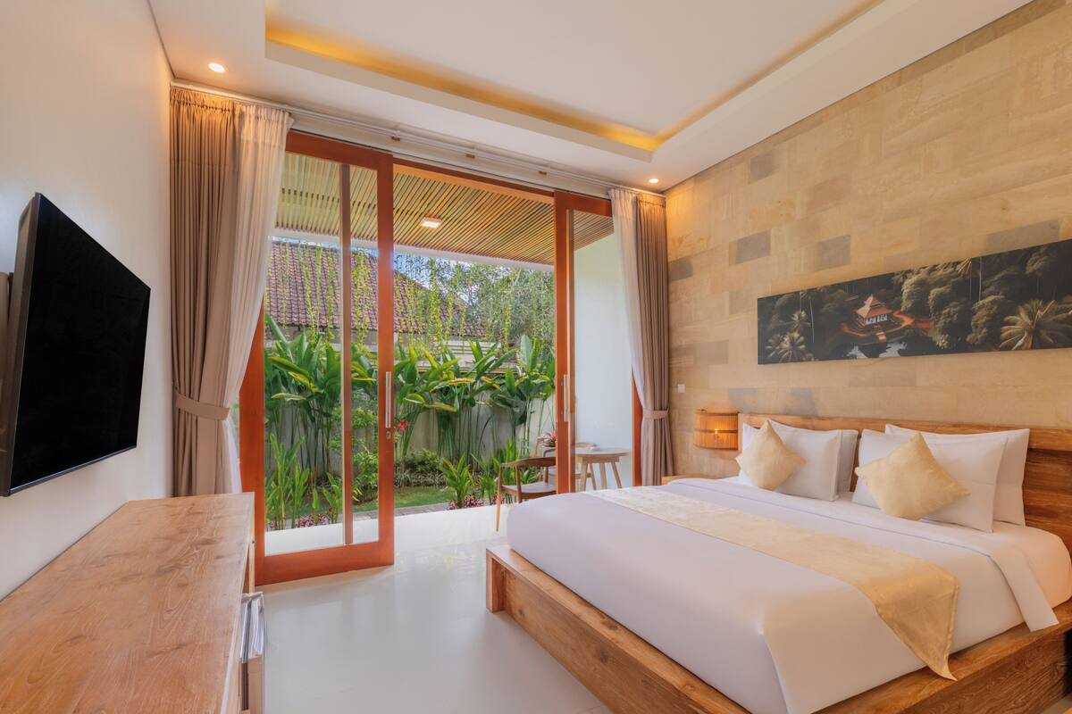 A modern bedroom with a large bed, a TV, and a sliding glass door leading to a garden.
