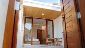 A modern hotel room with a wooden ceiling, a large sliding glass door, a bed, a desk, and a small pool area. - Bali Made Escape (Bangli)
