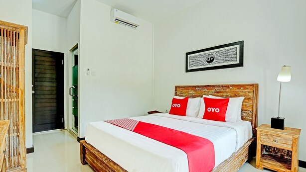 Ein ordentlich eingerichtetes Hotelzimmer mit einem großen Bett, einem Nachttisch, einer Wand-Klimaanlage und einem gerahmten Kunstwerk über dem Bett.
