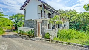 Une maison à deux étages dotée d’un balcon, entourée d’une végétation luxuriante.