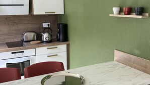 A modern kitchen with white cabinets, a marble countertop, and red chairs.