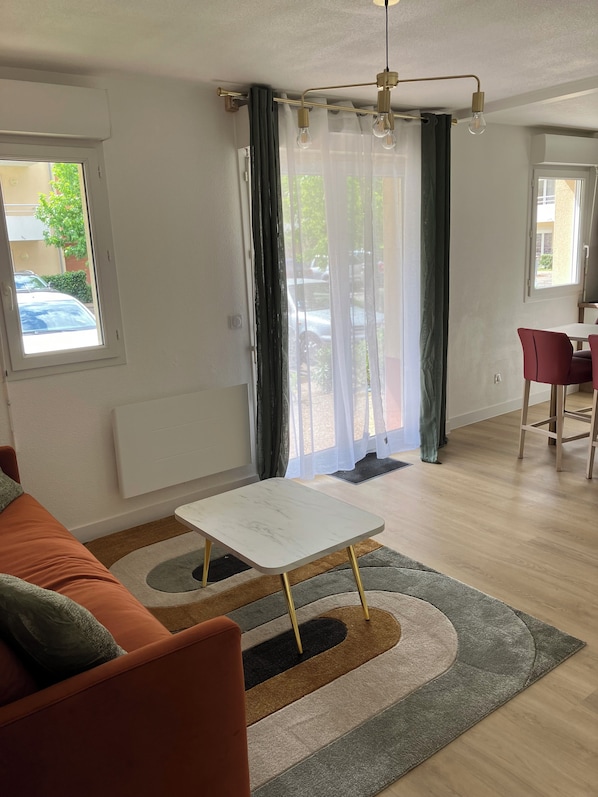 A modern living room with a sofa, a small table, and a dining area with chairs.