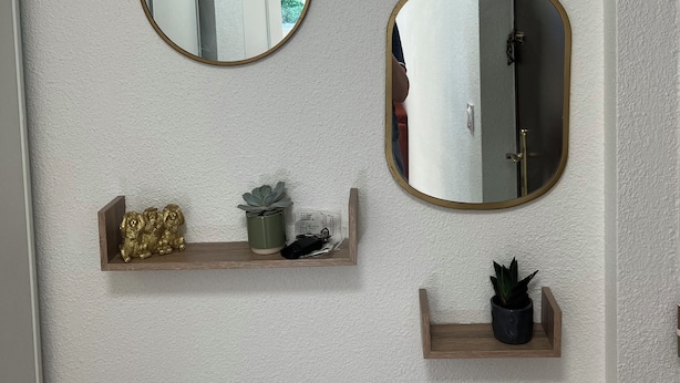 Three wall-mounted mirrors with gold frames, a wooden shelf with decorative items, and a potted plant.