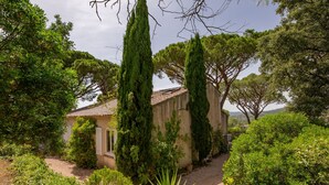 A rustic building surrounded by lush greenery, with tall cypress trees and a gravel path leading to the entrance. - Riviera by Interhome (Sainte Maxime)
