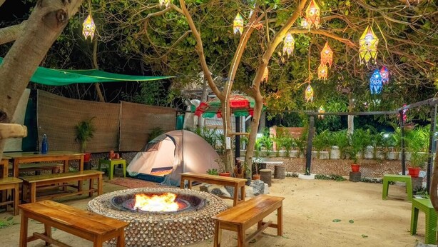An outdoor seating area with wooden tables and benches, a fire pit, and hanging lanterns. - Michael's Island Resort (Brahmagiri)