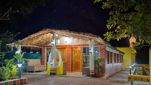 A small, two-story building with a thatched roof and brick walls, featuring a circular window and a wooden door. - Michael's Island Resort (Brahmagiri)