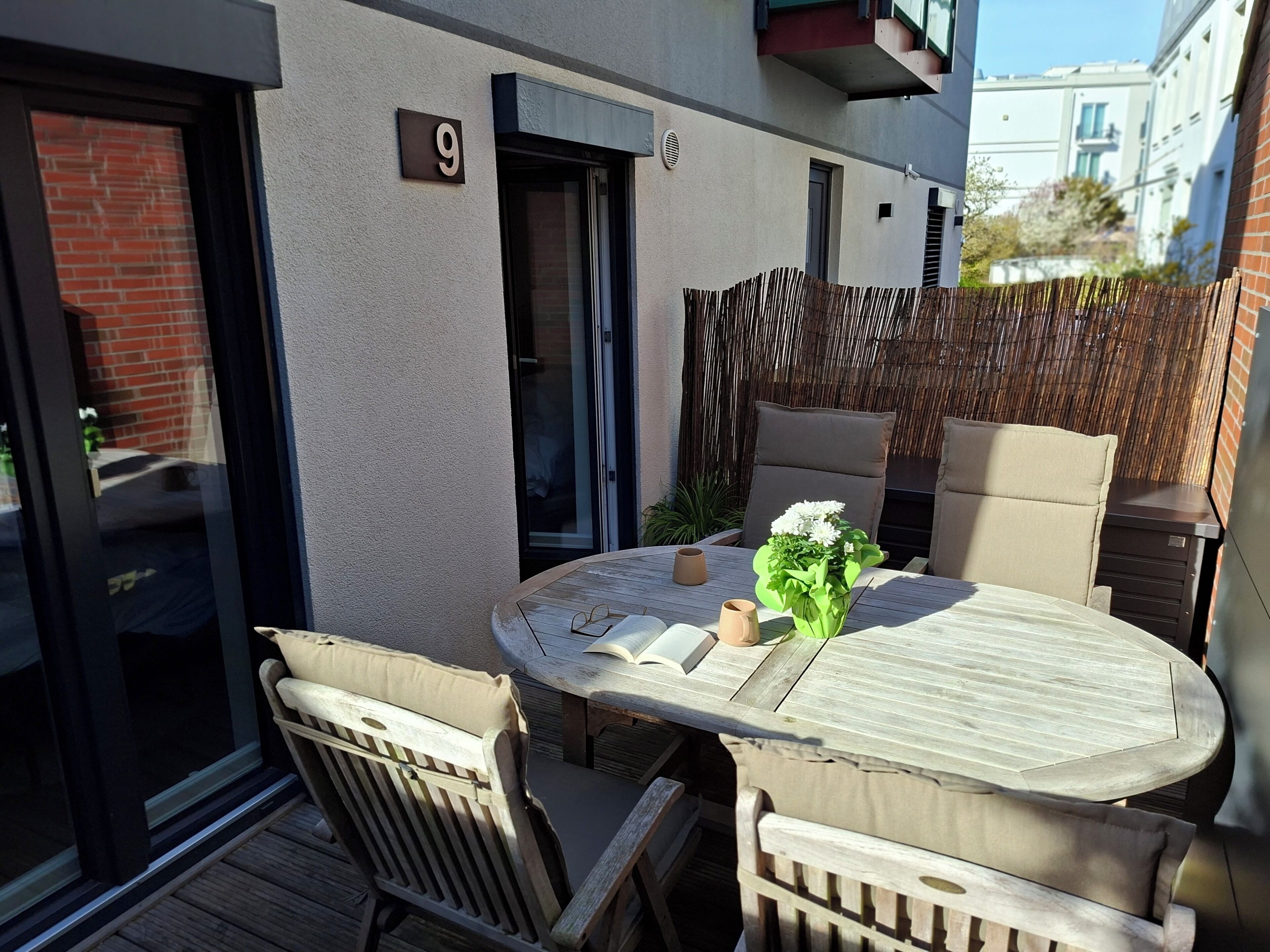 Eine Terrasse mit einem runden Tisch, zwei Stühlen, einem kleinen Blumentopf und einem Holzzaun.