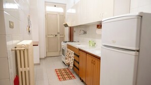 Una cuina amb armaris blancs, un frigorífic, una placa de cocció i un terra emblat.
