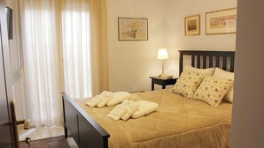 A neatly made bed with a beige duvet, a bedside lamp, and floral pillows. - Alkinoos Apt -Inspiring Living in Meteora -3BD (Kalampaka)