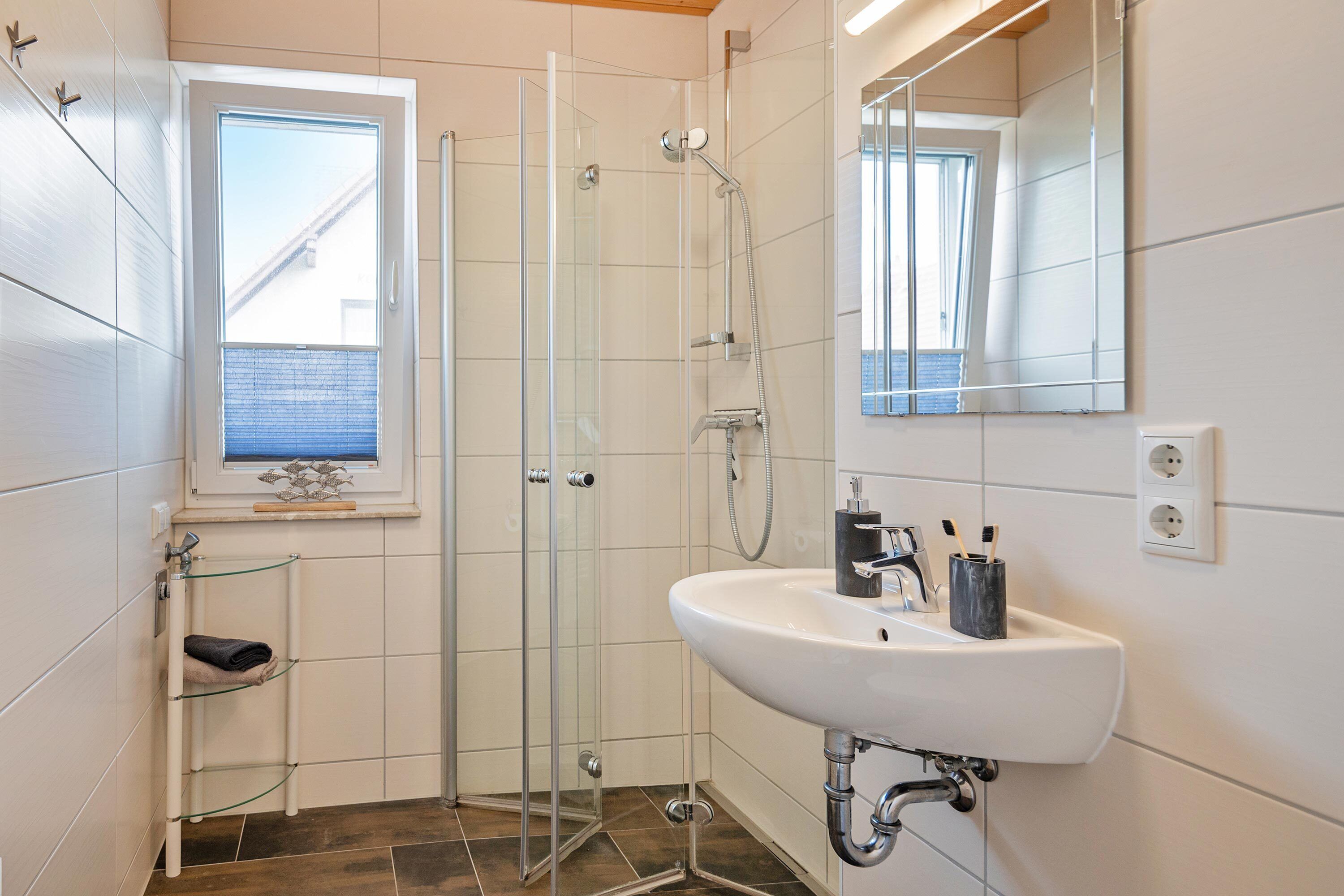 A modern bathroom with a glass-enclosed shower, a white sink, and a window.