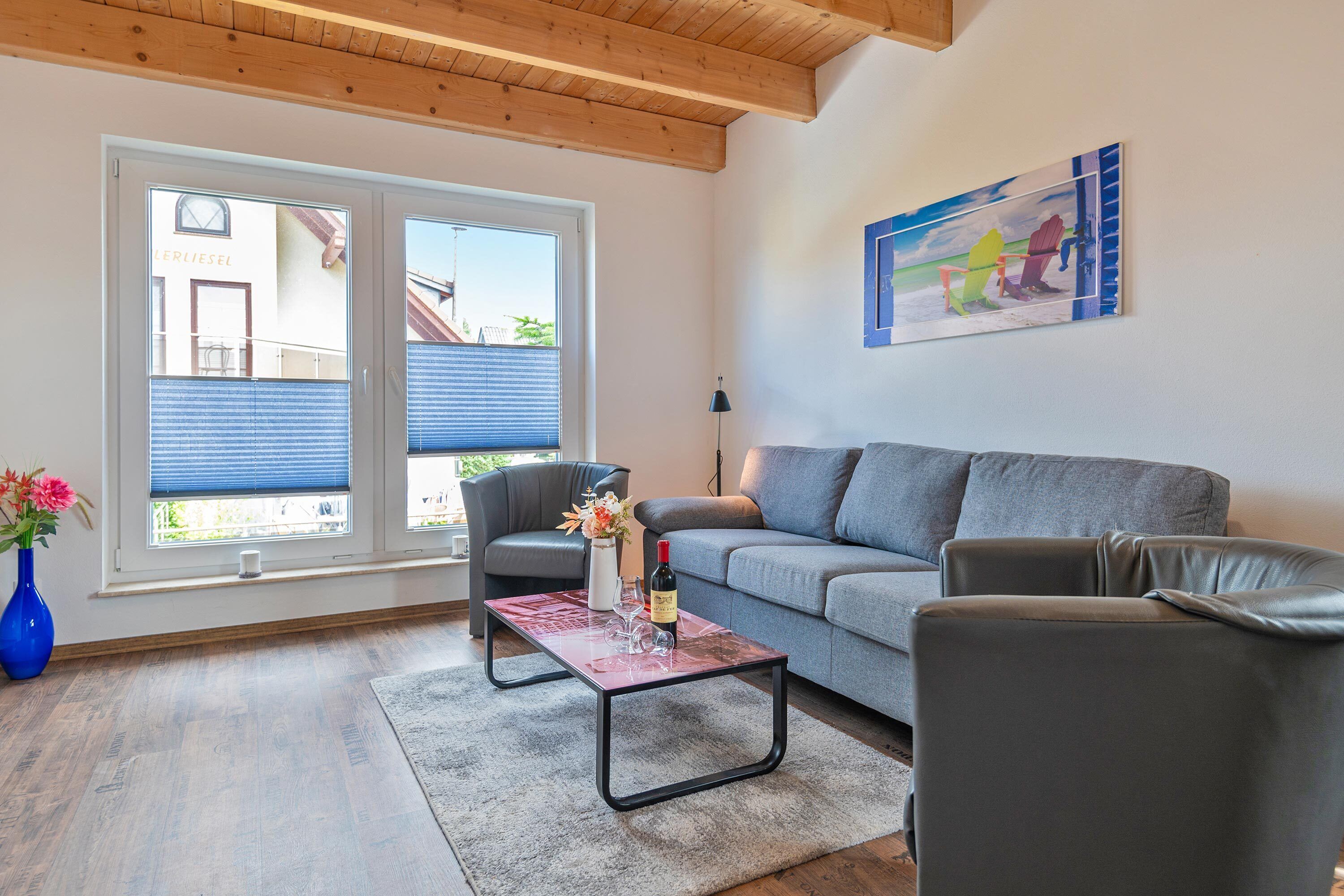 Ein modernes Wohnzimmer mit einem grauen Sofa, einem schwarzen Ledersessel, einem Couchtisch und einem Gemälde an der Wand.
