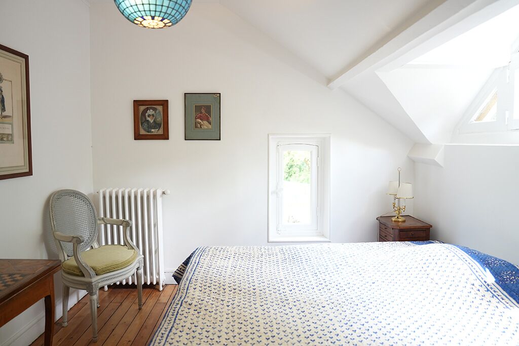 Un dormitorio con cama, una silla, un radiador, una ventana y una lámpara.