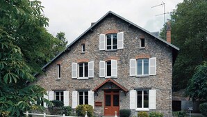 Ein Steinhaus mit einem zentralen Eingang, mehreren Fensterläden und einem weißen Zaun davor.