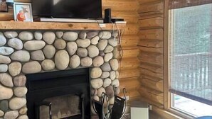 Une cheminée en pierre surmontée d’un téléviseur à écran plat, des murs en bois et une fenêtre avec des stores.