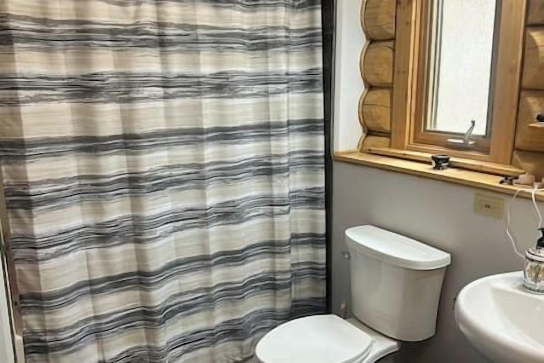 A bathroom with a striped shower curtain, a toilet, a sink, and a window with a wooden frame.