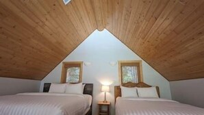 Une chambre avec deux lits, des poutres apparentes en bois au plafond et deux fenêtres.