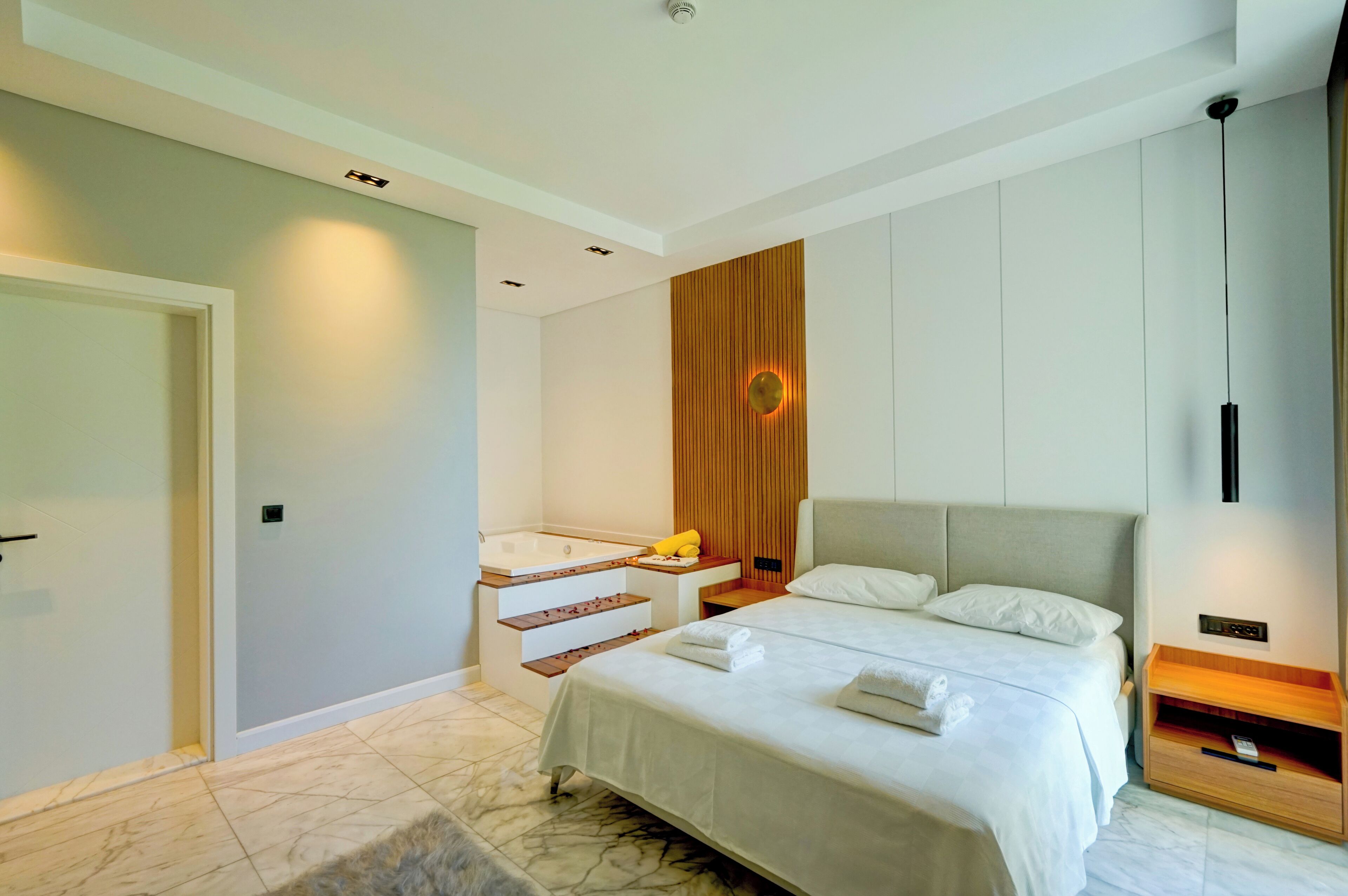 Una habitación de hotel moderna con una cama grande, una bañera empotrada y un panel de pared de madera.