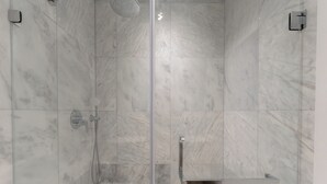 Eine moderne Dusche mit Glastür, Marmorwänden und einer integrierten Ablagefläche.