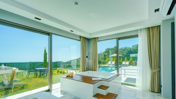 Ein modernes Badezimmer mit einer großen Badewanne, einem Holzausleger und Blick auf einen Pool und Grünflächen.