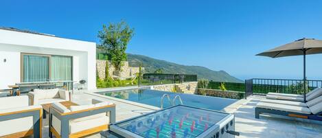 Zona junto a la piscina con mesa de fútbol de mesa, sillas de descanso y vistas al mar.