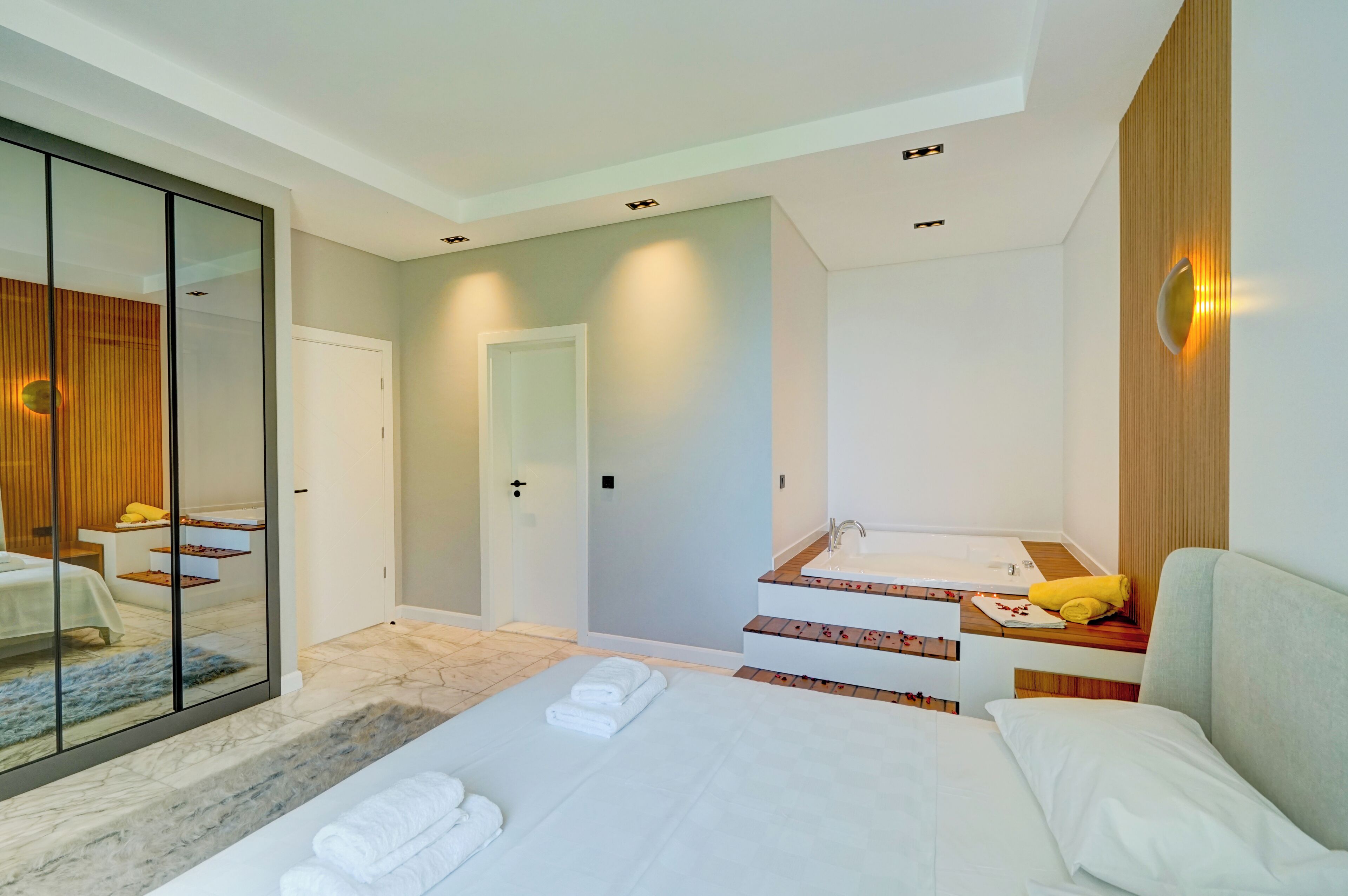 A modern hotel room with a large bed, a separate bathroom with a vanity, and a sliding glass door leading to a balcony.