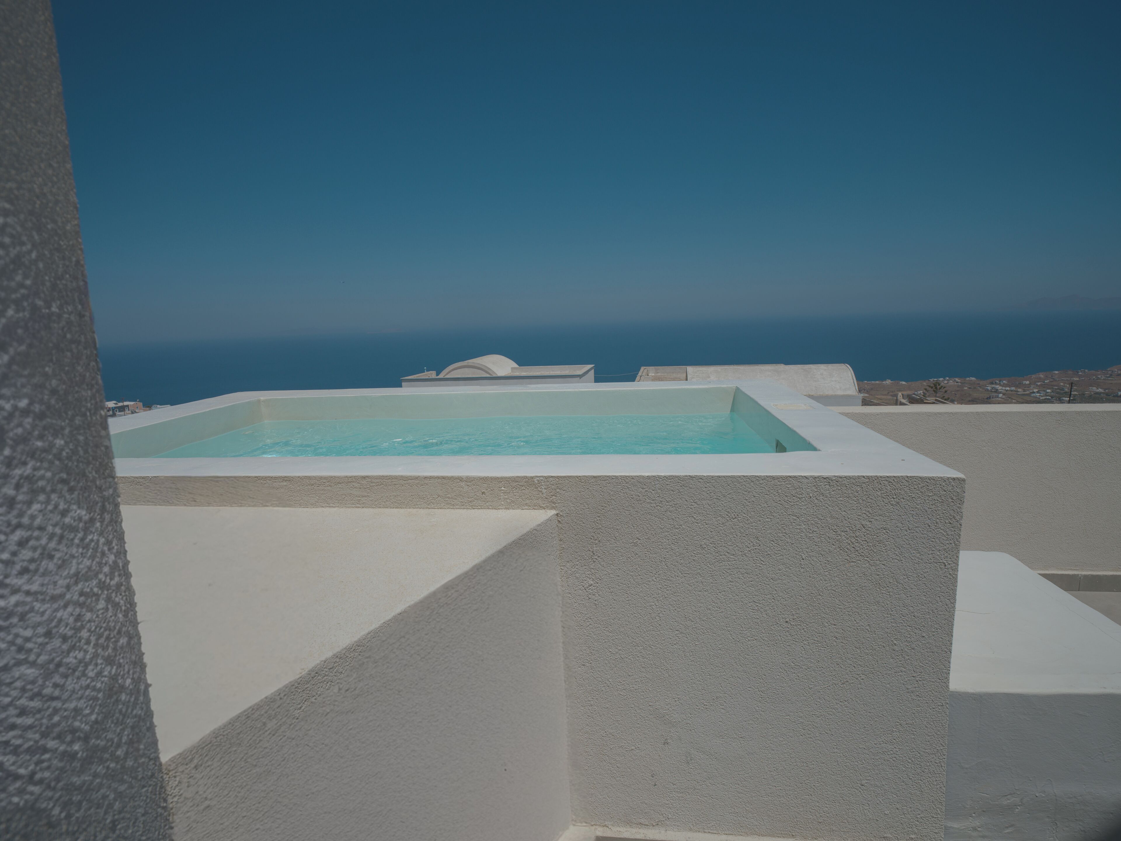 Une piscine rectangulaire à l’eau d’un bleu limpide, entourée de murs blancs, se détachant sur un ciel dégagé et un paysage lointain.