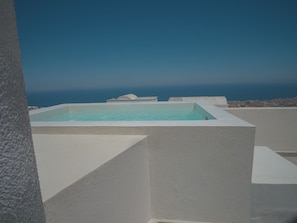 Una piscina rettangolare con superficie d'acqua cristallina e azzurra, circondata da pareti bianche, con sullo sfondo un cielo sereno e un paesaggio lontano.