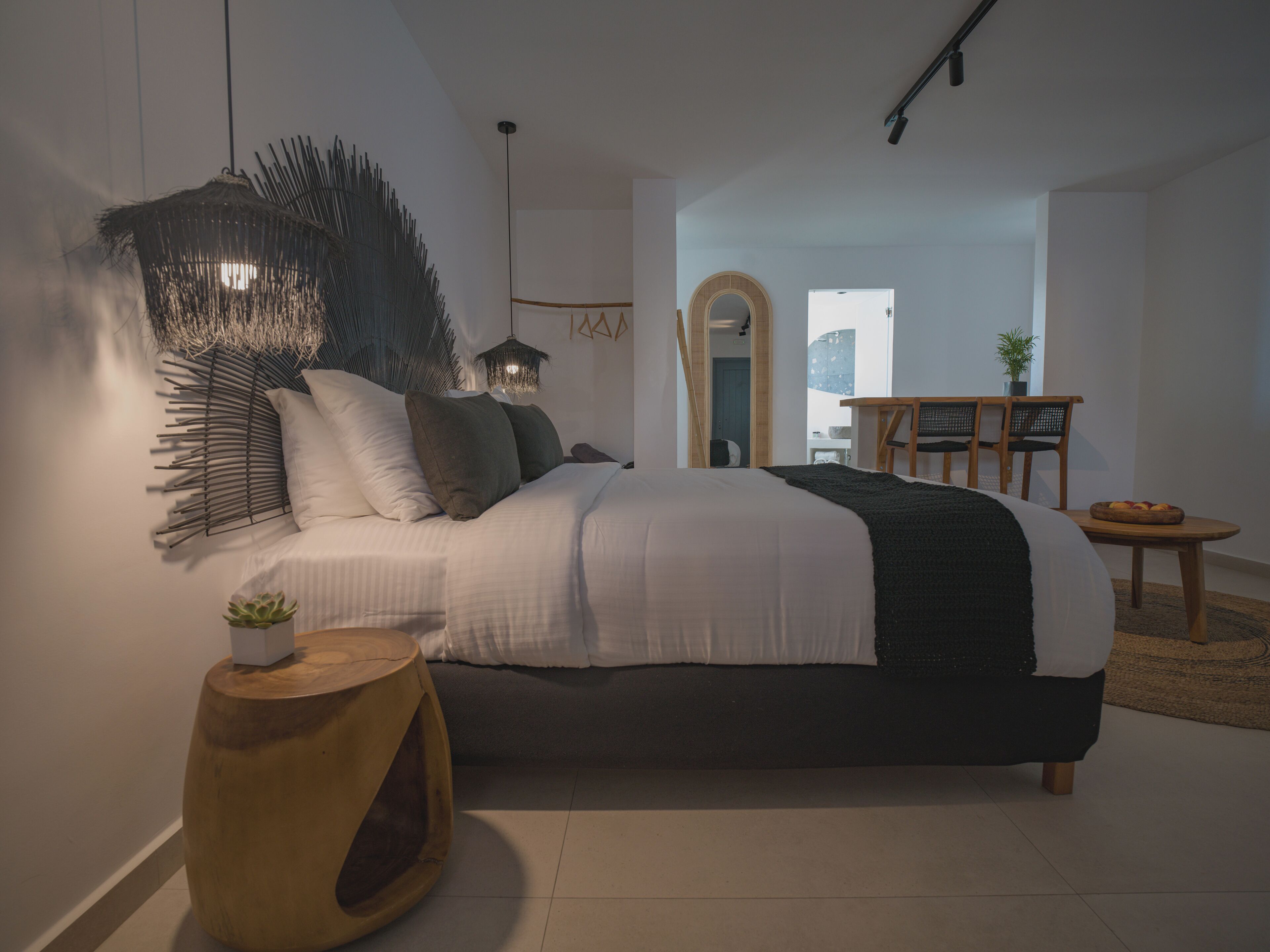 Un dormitorio moderno con una cama grande, una decoración de pared original, una mesita de madera pequeña y vistas de la ciudad a través de un arco.