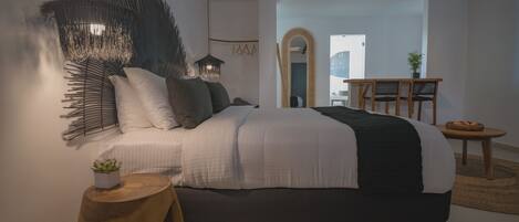 Un dormitorio moderno con una cama grande, una decoración de pared original, una mesita de madera pequeña y vistas de la ciudad a través de un arco.