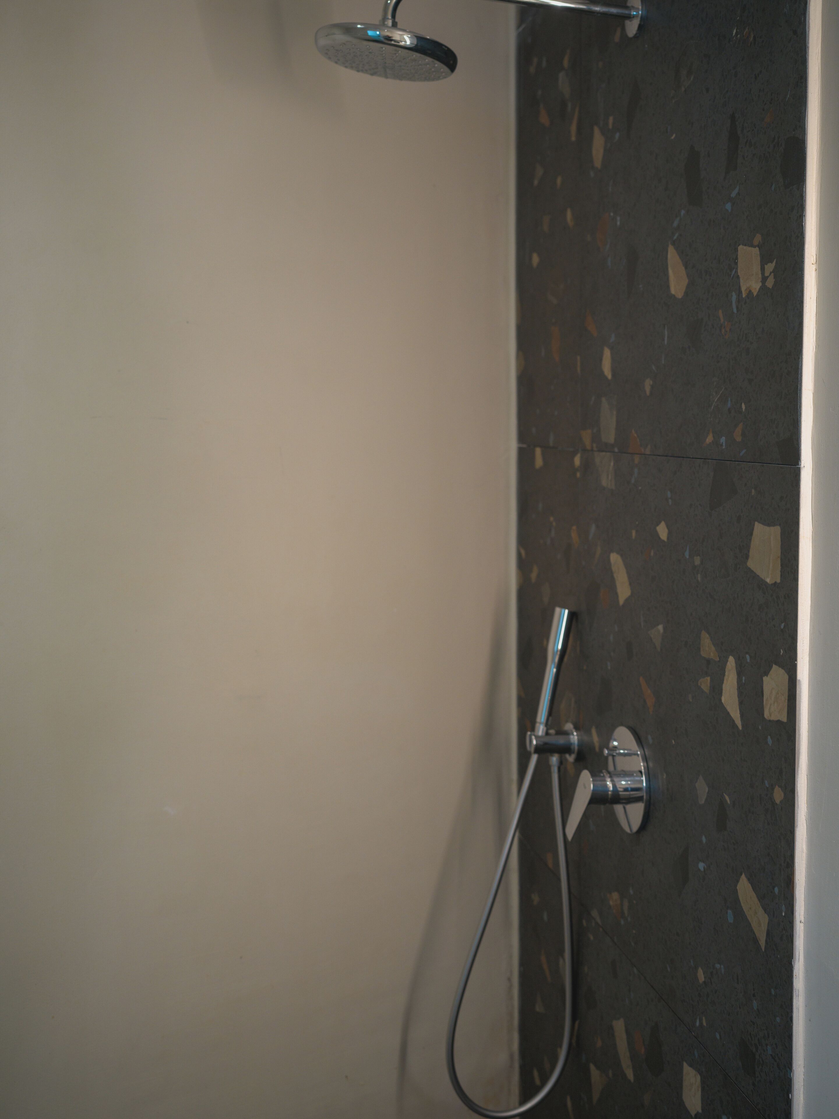 A shower area with a handheld showerhead and a wall-mounted faucet.