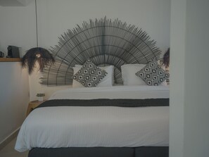 A bed with a unique curved headboard, a small potted plant, and patterned pillows. - Anemos Imerovigli Suites (Santorini)