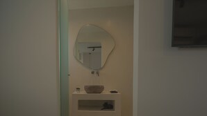 A bathroom with a large mirror, a wooden basin, and a shelf with a pair of shoes. - Anemos Imerovigli Suites (Santorini)